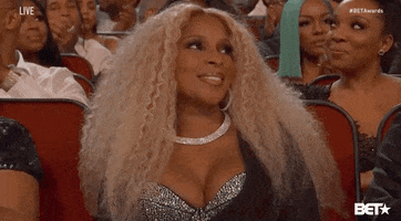 Celebrity gif. May J Blige in the audience of the 2019 BET awards looks around with a smile and then flips her blonde curly hair.