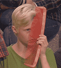 Video gif. A young boy is combing his hair with a comically large comb that is three times the size of his head. He brushes his bangs calmly and looks unfazed.