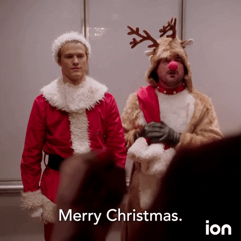TV gif. Lucas Till as MacGyver, dressed as Santa Claus, and George Eads as Jack, dressed as Rudolph, are frozen in alarm by an unseen, unexpected guest. Jack as Rudolph waves and says “Merry Christmas.”