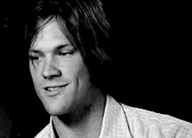 Celebrity gif. Jared Padalecki seductively bites his lip at us and licks his fingers to sexily slick back his hair.