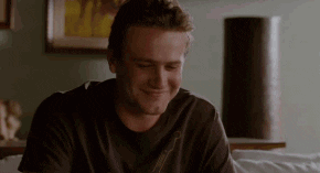 Movie gif. Wearing a brown t-shirt, Jason Segel tilts his head and playfully shrugs at us.