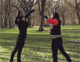 Video gif. In slow motion, two people jump towards each other with both feet kicked up and high five each other.