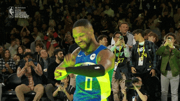 Sports gif. Damian Lillard of the Portland Trail Blazers is at the NBA All-Star Game. He's walking out onto the court as he looks down at his wrist and taps it twice. 