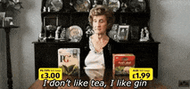 Video gif. Old woman sits at a table with two boxes of tea in front of her. She pulls a glass out from behind the boxes and says spicily, “I don’t like tea; I like gin.”