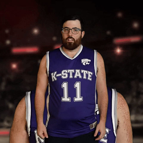 Video gif. Double take of a man wearing a Kansas State basketball jersey and glasses edited to be standing one in front of the other holding his arms out and making spirit fingers. He is a bit out-of-shape wearing glasses, mouthing the text that pans across the bottom of the screen with a deadpan expression, "Ohhhh'