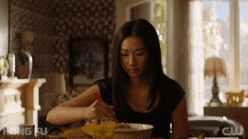 TV gif. Olivia Liang as Nicky Shen in Kung Fu takes a bite of a dumpling while looking around the room.