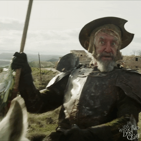 Movie gif. Jean Rochefort as Don Quichotte in The Man Who Killed Don Quixote rides a horse and holds a flag pole in one hand bobs his head around as he says, “Me, me, me, me.” Adam Driver as Toby Grummett stares at him with an annoyed expression.
