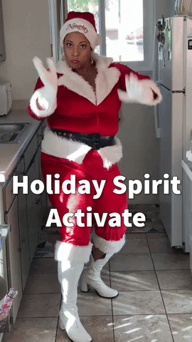 Video gif. Woman in a Santa costume claps her hands in front of her face at us and does a sassy dance in a kitchen. Text, "Holiday Spirit Activate."