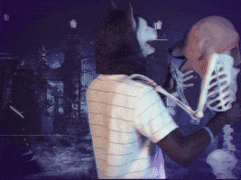 Video gif. Man wearing a werewolf mask is slow dancing with a skeleton that has a Golden Retriever mask on.