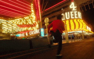 Music video gif. From the video for "Heartless", The Weeknd runs frantically past bright casino entrances wearing sunglasses and a pink jacket.