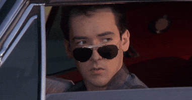 Movie gif. John Cusack as Lane Meyer in Better Off Dead has his car window rolled down and he looks out of it, tilting on his nose. He winks dramatically, moving his mouth open to exaggerate the wink.