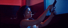 Music video gif. Cardi B in her video for Press. A cigarette dangles from her lips as she leans back and cocks a gun.