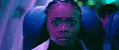 Music video gif. Skai Jackson in Lil Nas X's Panini video has a petrified look on her face, accentuated by ambient purple lighting, and she bolts out of her airplane seat.