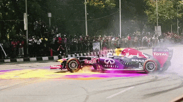 Sports gif. A race car spins around in a circle on top of pink and yellow pigments, spreading huge clouds of colorful dust in the air.
