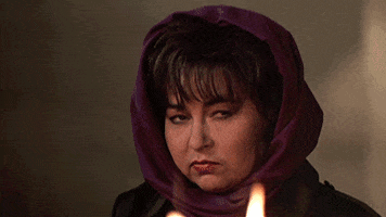 TV gif. Roseanne Barr as Rosanne stares offscreen as fire crackles in front of her.