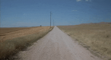 Movie gif. Jon Heder in Napoleon Dynamite runs with head down along the middle of a desolate gravel road in the middle of nowhere.
