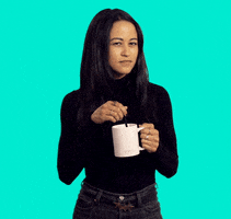 Celebrity gif. In front of a solid cyan background, wearing a black sweater and jeans, Hillary Gilmore stirs a white mug while squinting at us with low-key suspicion.