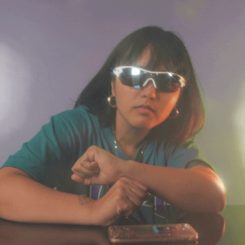 Video gif. Young woman wearing sunglasses and vibing with her elbows on the tabletop.