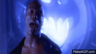 An animated GIF of Seal in the music video Kiss from a Rose. He stands in front of a giant light (the bat signal from Batman Forever) and sings.