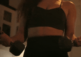 Video gif. We see the torso of a woman wearing workout clothing as she lifts two dumbbells in either hand at her waist.