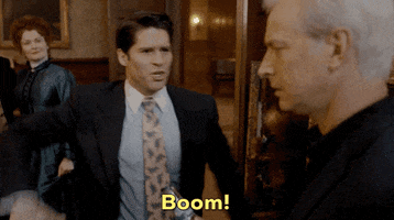 TV gif. A scene from Ghosts: While Rebecca Wisocky as Hetty looks on, Asher Grodman as Trevor makes a throwing motion and shouts tauntingly at Rob Huebel as Ari. Text, "Boom!"