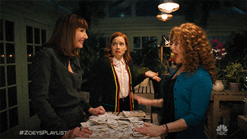 TV gif. Mary Steenburgen as Maggie, Bernadette Peters as Deb, and Jane Levy as Zoey on Zoey's Extraordinary Playlist are all gathered around a table of cash and Maggie and Deb high five one another excitedly.