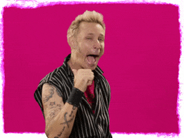 Celebrity gif. Mike Dirnt from Green Day stares at us with a turtle-like smile, covering his teeth with his lips. He raises up a big thumbs up. 