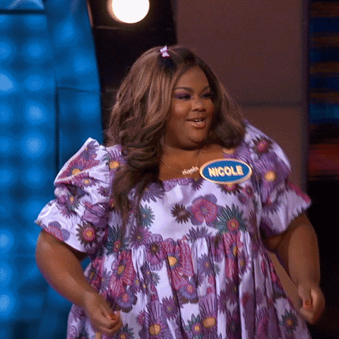 TV gif. Contestant on "Celebrity Family Feud" wearing a floral dress and a blue contestant badge walks forward and shimmies with a seductive expression on her face as lights from the set twinkle behind her. 