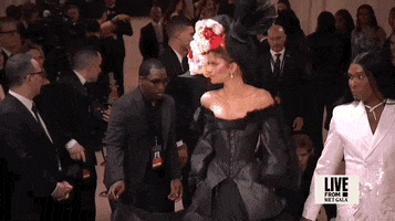 Met Gala 2024 gif. Zendaya sashays in wearing an all-black vintage Givenchy 1996 Couture gown and a big floral hat as we zoom out to reveal the whole look.