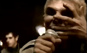 Music video gif. Gerard Way, lead singer of My Chemical Romance, in their video for Famous Last Words. He clutches his face with one hand and pulls at his skin while singing into the mic.