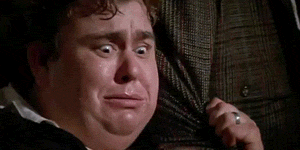 Movie gif. We see a close-up shot of John Candy grabbing at the arm of a suit on a hanger, scared and looking for a place to hide.