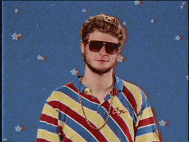 Video gif. A white man with curly, sandy blonde hair and a scruffy beard wears a striped shirt and dark brown sunglasses. He points a finger straight ahead, then nods and grins wide as animated stars twinkle behind him.