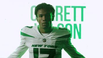 Video gif. New York Jets football player Garrett Wilson wears his team jersey and stands with his arms crossed and nods with confidence in front of a screen with a montage of graphics for the New York Jets.