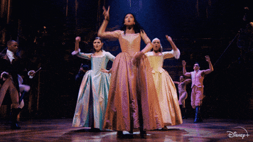 Celebrity gif. Phillipa Soo, Jasmine Cephas Jones, and Renee Elise Goldsberry standing in a triangular formation, as the Schuyler Sisters in Hamilton, pump their fists in the air excitedly.