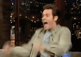 Celebrity gif. Jim Carrey pumps his fist in celebration on a late night show, then pulls confetti from his pocket and throws it everywhere. Next he blows on a kazoo then drinks from a mug and spits it out forcefully and shakes hands with the host. Then he runs to the camera and spins around with it, then runs into the audience, grabs a woman, and pretends to make out with her. Then he finds a man in the audience, pretends to kiss him on the ground, then runs to hug someone else, then back to the man and kisses him again.