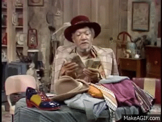 TV gif. Redd Foxx as Fred G. Sanford on Sanford and Son counts a fat stack of money in an ornate hat, surrounded by his shopping.