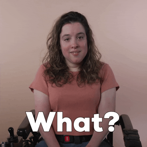 Reaction gif. A Disabled white-presenting Latina woman with cerebral palsy and kinky-curly brown hair, seated in her motorized wheelchair, cocks her head and asks deliberately, "What?"
