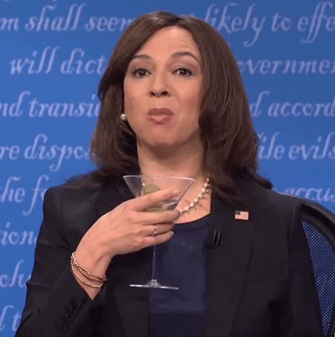 SNL gif. Maya Rudolph as Kamala Harris holds a half-empty martini glass which catches some of the drink that is spilling out of her mouth as she does a spit take.