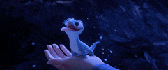 Disney gif. Bruni, Princess Elsa's salamander, in Frozen II, sits in Elsa's palm, catching a snowflake on his tongue and gobbling it up happily.  