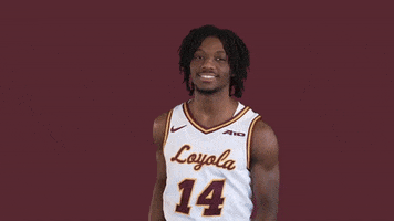 Sports gif. Loyola Ramblers basketball player Caleb Reese stands in front of a maroon background grinning. He makes two rings with his thumb and forefinger and puts his hands up to his face to make glasses. Then, he pretends to grab a bow and arrow from a quiver on his back and shoots it at us.