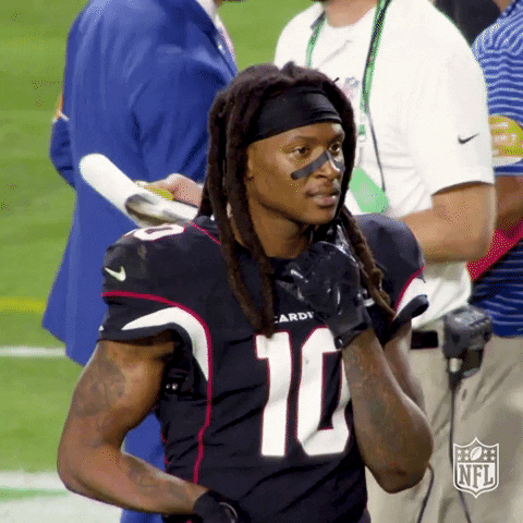 NFL gif. Arizona Cardinals wide receiver DeAndre Hopkins stands on the football field holding the collar of his jersey. "Damn," he says, disappointed. Text: "Damn."