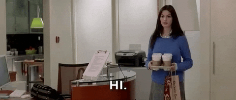 Anne Hathaway saludando con vasos de café en la mano