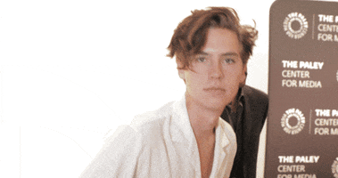 Celebrity gif. Cole Sprouse at the Paley Center for Media looks at us and does one big wave from left to right.