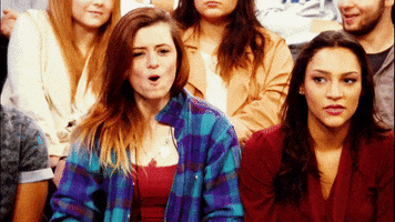 Reality TV gif. Two girls in the audience of Maury pop up, cheering.