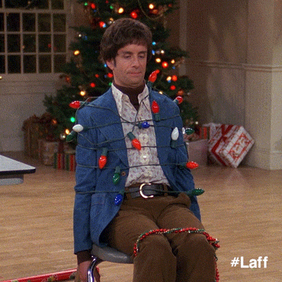 TV gif. A man clad in retro clothes from That 70s Show is tied up to a chair with Christmas lights. The lights blink as he looks unamused.