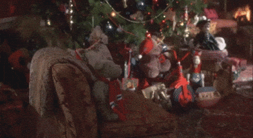 Video gif. We pan over a living room with a beautifully decorated Christmas tree in front of a fire burning in the fireplace.