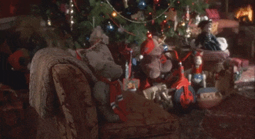 Video gif. We pan over a living room with a beautifully decorated Christmas tree in front of a fire burning in the fireplace.