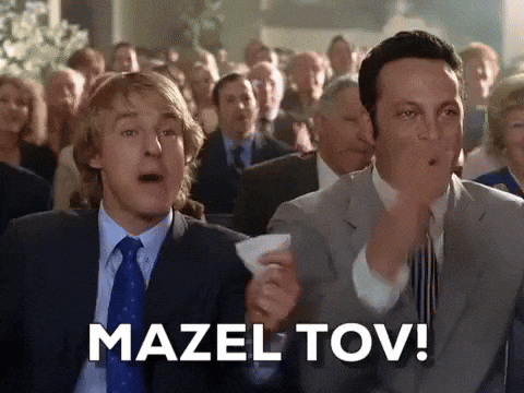 Movie gif. Owen Wilson as John and Vince Vaughn as Jeremy in Wedding Crashers genuinely cheering with the rest of the crowd at some big wedding moment. Text, "Mazel Tov!"