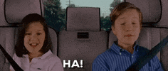 Movie gif. Elizabeth Yozamp as Tiffany and Lurie Poston as Tommy in Step Brothers. They sit in a car together and lean sideways towards the middle seat, saying "Ha!" in unison and looking very symmetrical.