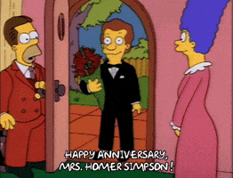 The Simpsons gif. Homer (with hair) wears a brown suit as he holds the back door open. Marge stands nearby in her nightgown, pleasantly surprised, as a man in a tuxedo holding a bouquet enters to exclaim: Text, "Happy anniversary, Mrs. Homer Simpson!"